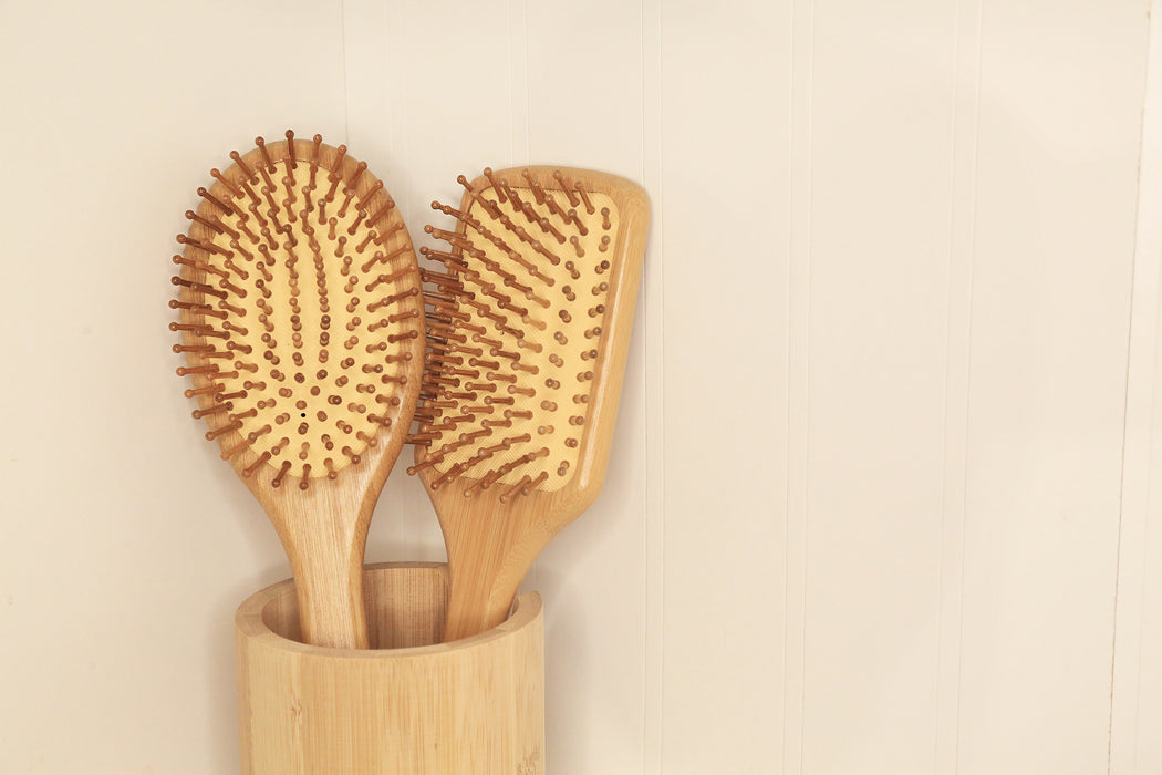Oval and rectangular cushioned bamboo hair brushes in a bamboo case, and minimal background.