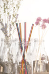 Multicolor stainless steel straws placed in glass jar with colorful florals at the back.