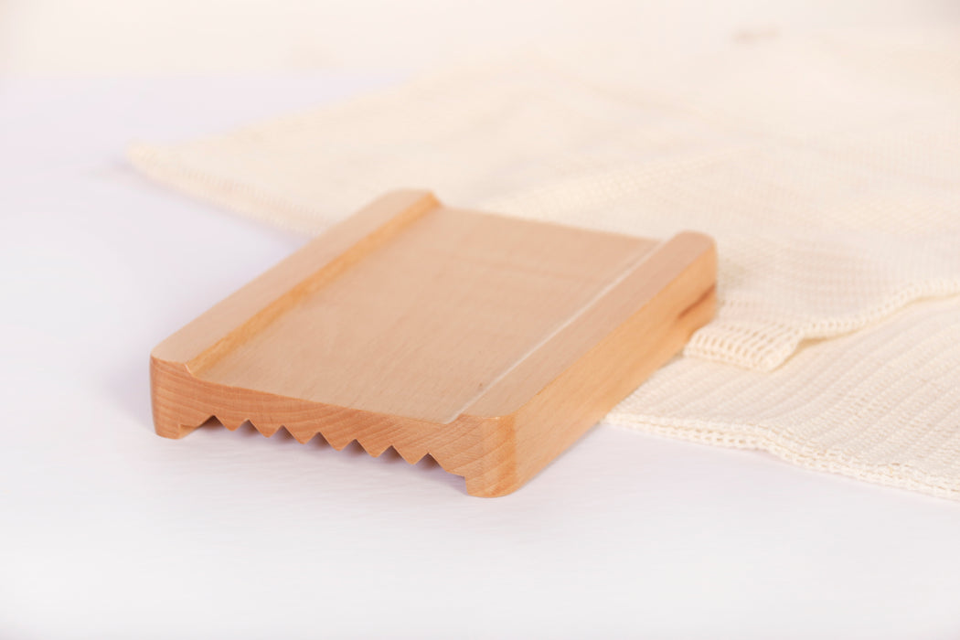 Natural bamboo soap dish with cotton mesh and white background. Features reversible sides, with flat side facing up, and ridged side facing down.