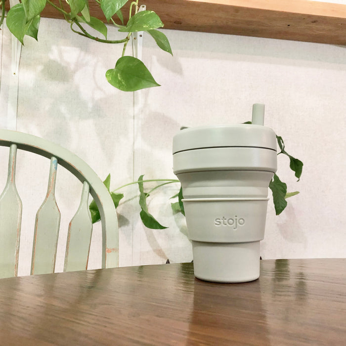 Sage color Stojo cup in 16oz. on the table with sage theme coordinate background..