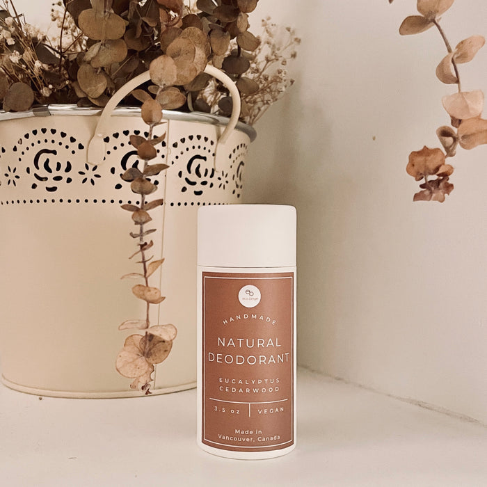 Handmade natural deodorant container with a decorative vase and dried eucalyptus on a light background