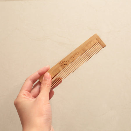 Eco Beige travel size bamboo comb held at cream background.