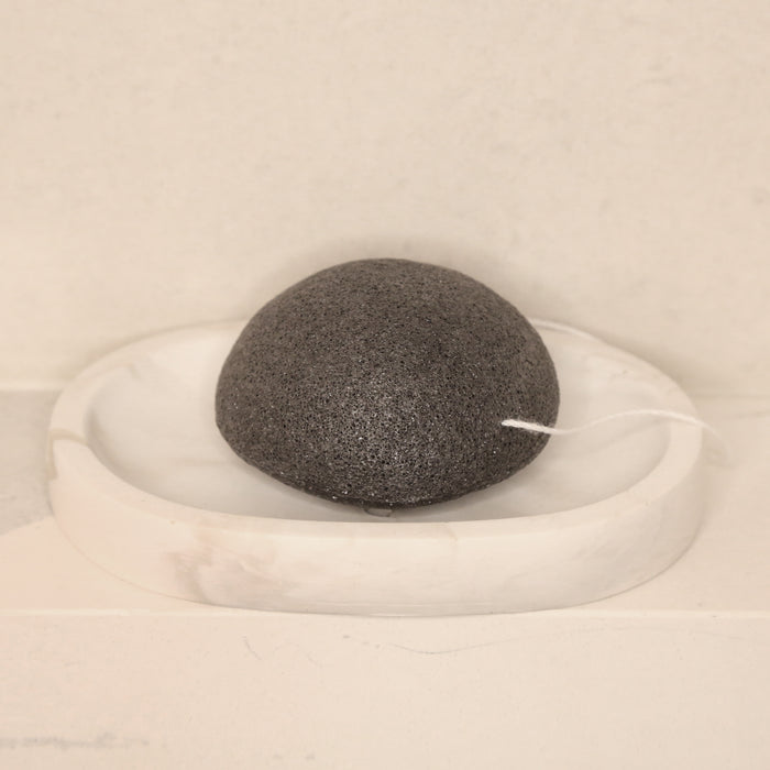 Charcoal Konjac Sponge on marble concrete tray sitting on shower counter.