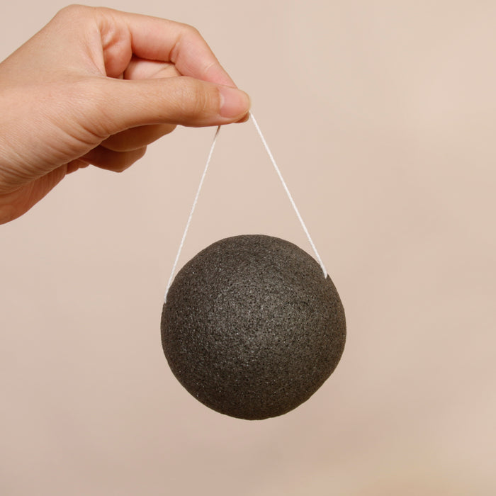 Charcoal Konjac Sponge hand held with string attached. Clean minimal background.