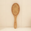 Oval cushioned bamboo hair brush with Eco Beige engraved on the handle.  Standing straight again a white wall.