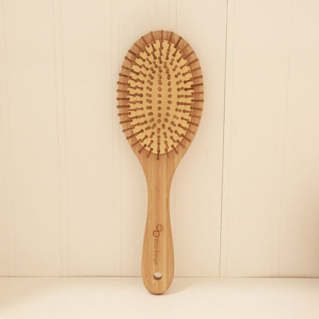 Oval cushioned bamboo hair brush with Eco Beige engraved on the handle.  Standing straight again a white wall.