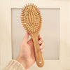Oval cushioned bamboo hair brush with Eco Beige engraved on the handle. Hand held in minimal background.