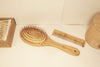Oval cushioned bamboo hair brush with Eco Beige engraved on the handle. Placed along other bamboo bathroom products.