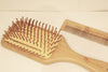 Rectangular cushioned bamboo hair brush with Eco Beige engraved on the handle. Bamboo comb on the side with minimal background.