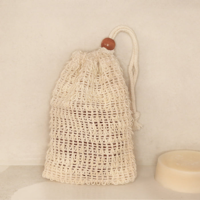 Natural sisal soap saver bag on shower counter with soap inside and on the side.
