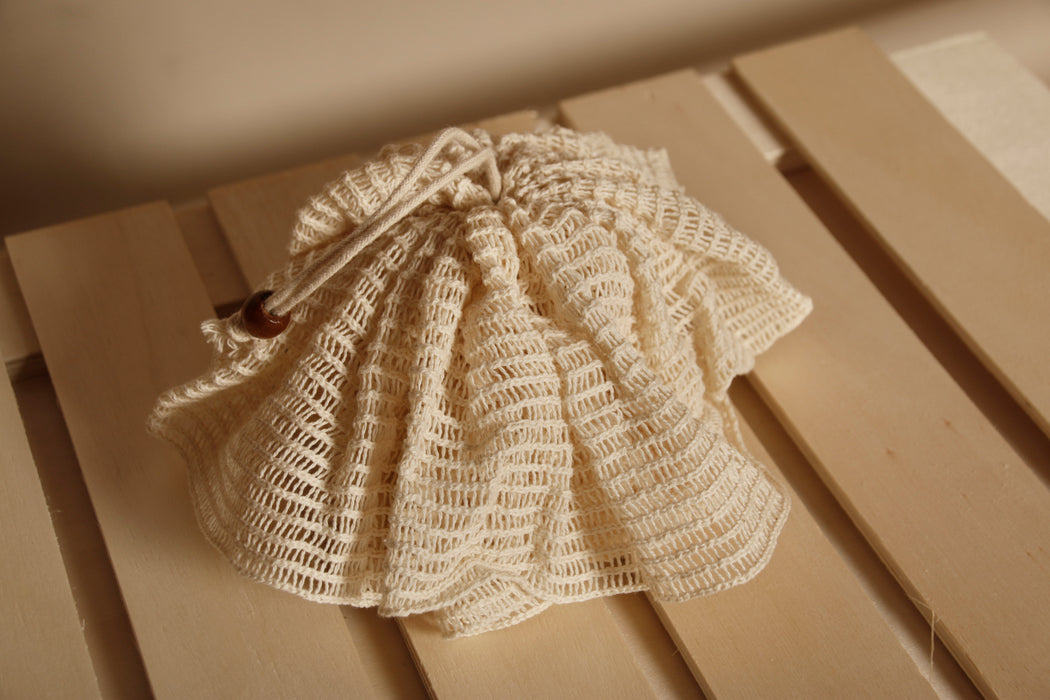 Natural ramie bath pompom placed on wooden plank and in a neutral beige color background.