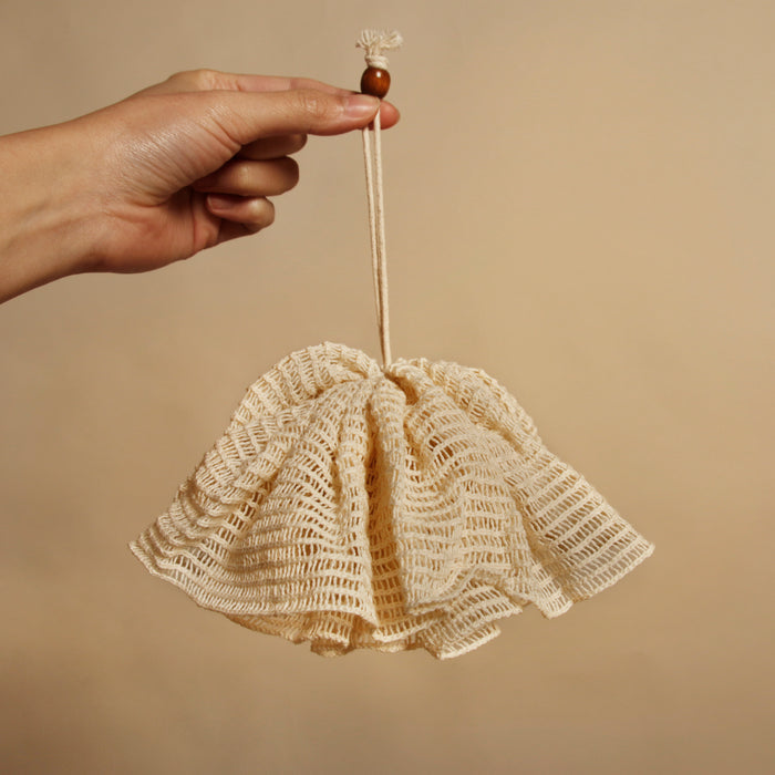 Natural ramie bath pompom hand held with string attached in a beige minimal background.