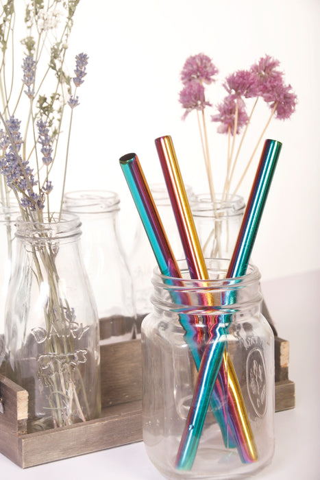 Multicolor stainless steel boba straws placed in glass jar with colorful florals at the back.