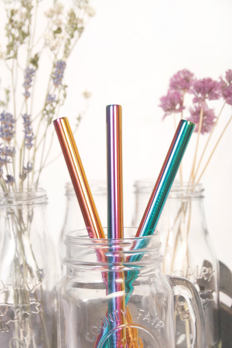 Multicolor stainless steel boba straws placed in glass jar with colorful florals at the back.