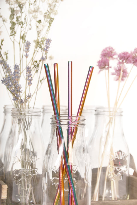Multicolor stainless steel straws placed in glass jar with colorful florals at the back.