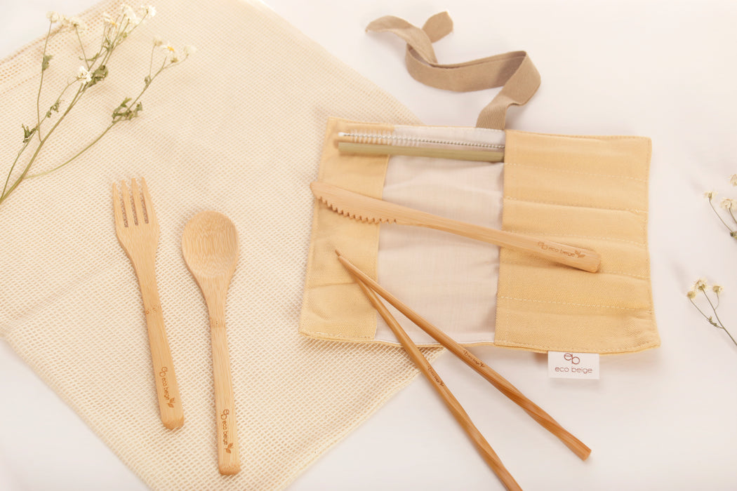 Eco Beige bamboo cutlery set with creamy color cotton fabric pouch and brown ribbon tapes attached. Set includes 6 pieces logo engraved cutleries ; spoon, fork, knife, chopstick, straw, and straw brush. White background with cotton mesh fabric and small white flowers..