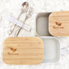 White and Neutral Grey Eco Beige bamboo lunch box with engraved logo on the lid. Lunch box opened view with lid half on the top. Comes with white elastic strap to hold utensils. Container made with wheat fiber and bamboo fiber. Marbled minimal background.