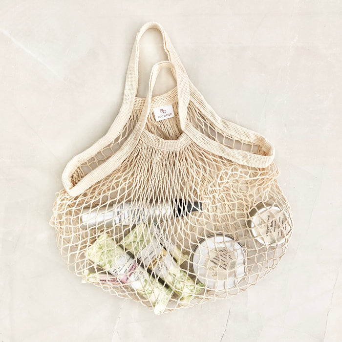 Eco Beige cotton netted hand bag flat layed with cosmetic products inside, and light color stoned background.