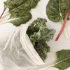 Eco Beige large cotton mesh produce bag with bunch kale leaves inside. Colorful Swiss chards scattered on the side.