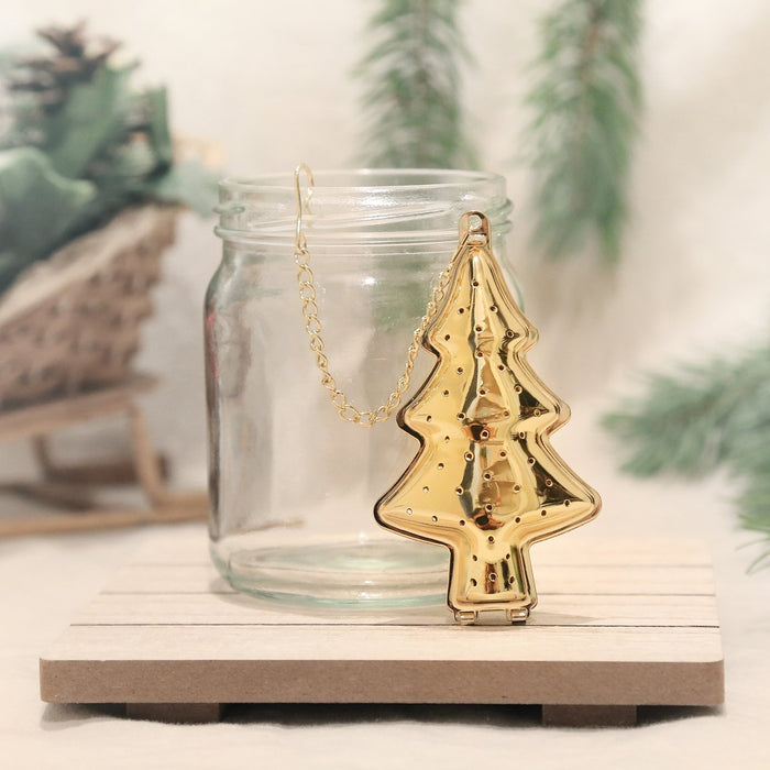 Gold Christmas Tree tea infuser with chain hanging from a glass jar. Holiday season theme background.