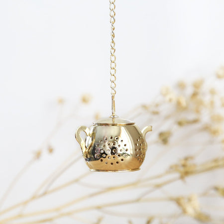 Mini Gold Teapot Tea Infuser with chain hanging at elegant and minimal background.