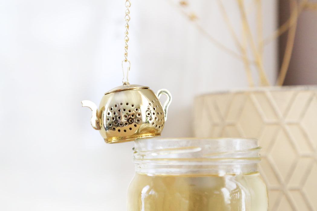 Mini Gold Teapot Tea Infuser with chain hanging at the edge of a jar with tea inside.
