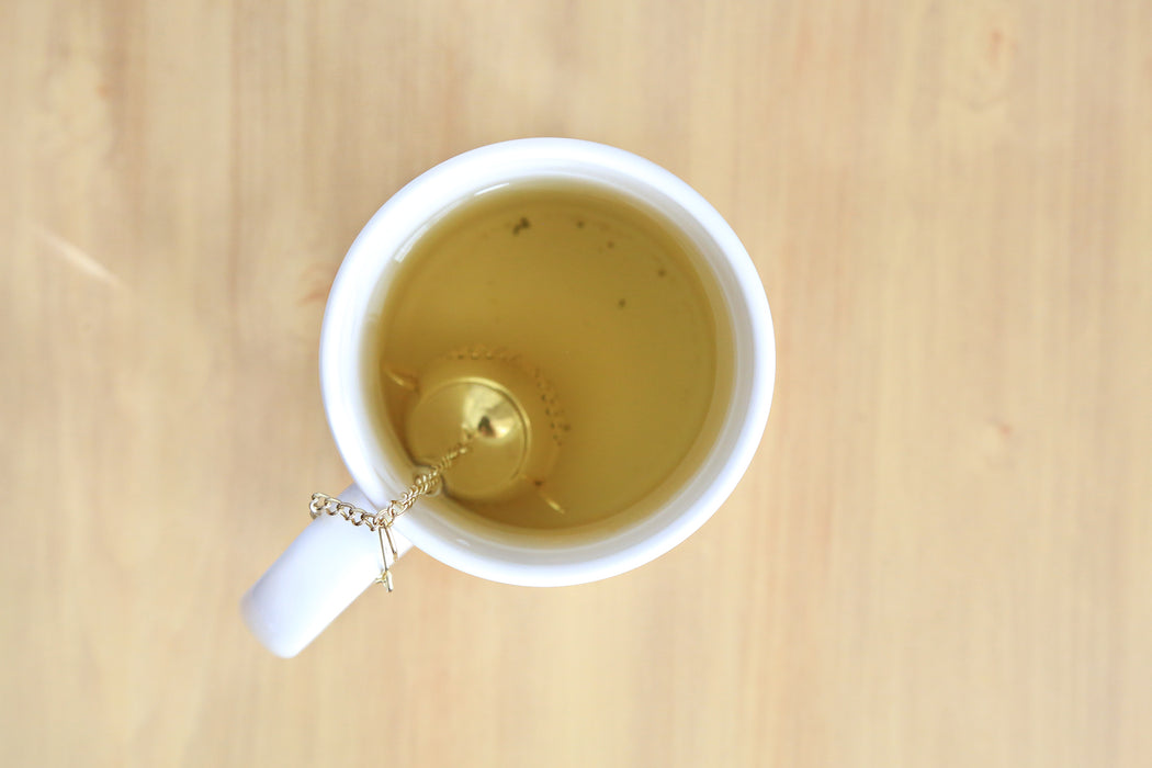 Mini Gold Teapot Tea Infuser immerged in a mug of tea with chains hooked on the mug handle. 