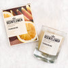 Scentlemen Studio hand poured soy wax tangerine scent candle in a glass container and candle box package. White crumbled paper background. 