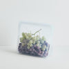 Stasher platinum silicone reusable clear stand-up mid bag storing grapes. In white background.