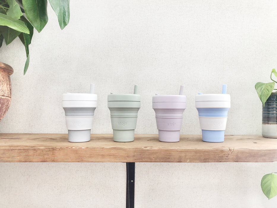 Multiple color 16oz Stojo cups on the shelf, with natural plant and beige wall background.